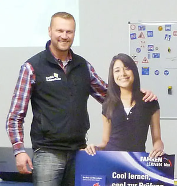 Fahrlehrer Andreas Gutbrod in der Fahrschule neben einer Fahrschülerin, im Hintergrund Lernplakate