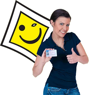 Junge Frau zeigt lachend ihren Führerschein vor dem Fahrschulschild mit Smiley