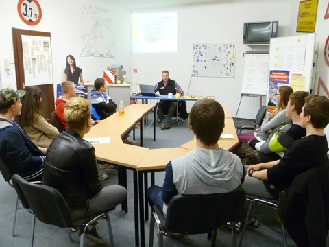 Fahrschülergruppe verfolgt den Theorieunterricht, an der Wand hängen Verkehrszeichen